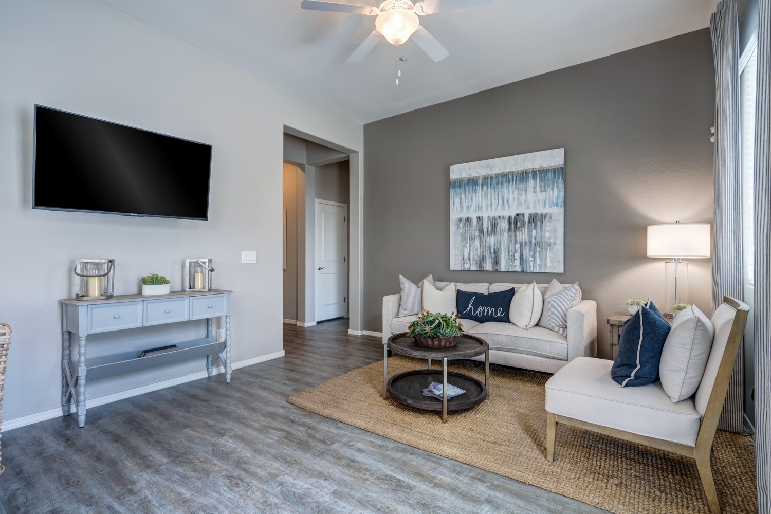 A living room with a white couch, a grey table, and a flat screen TV mounted on the wall.
